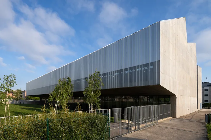 Cantilevered corrugated metal facade with horizontal band of windows above a planted lawn with young trees