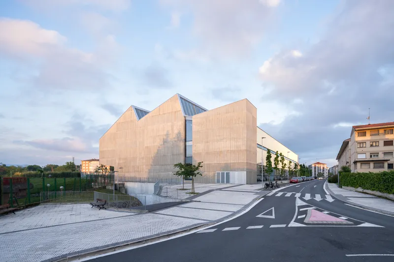 Timber-clad volumes with sawtooth glazed clerestory seen from the street at dusk under cloudy skies