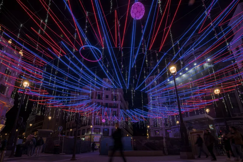 Overhead installation of radiating red and blue LED light tubes spanning a public square at night