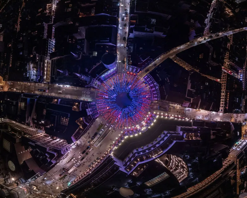 Aerial view of circular light installation with radiating blue and red tubes extending into surrounding streets