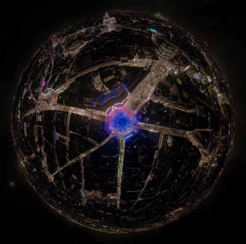 Fisheye aerial view of illuminated radial plaza with blue LED center and surrounding urban blocks at night