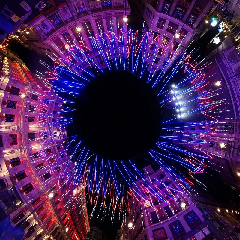 Overhead view into circular courtyard with radiating blue and red LED strands converging toward central void