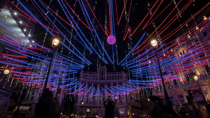 Radial array of suspended LED light tubes converging at a central pendant sphere above surrounding historic facades