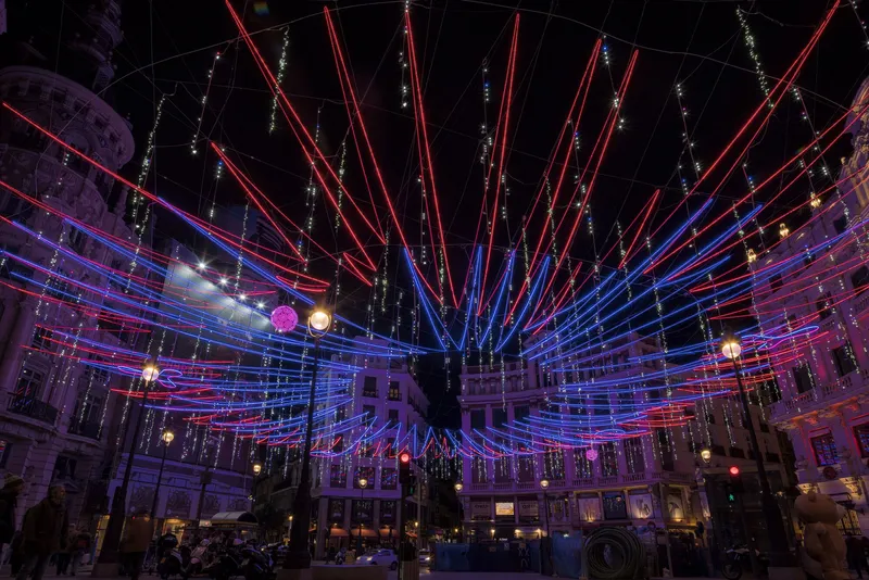Wide-angle view of the illuminated canopy installation spanning across the plaza with pedestrians gathered below at dusk