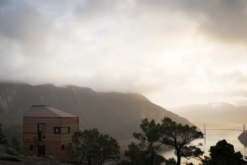 Timber-clad volume with gabled roof set against a mountainside under heavy cloud