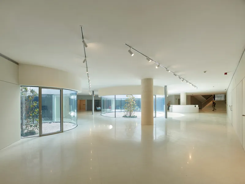 Interior lobby with polished floors, cylindrical column, curved glass wall overlooking a courtyard, and track lighting
