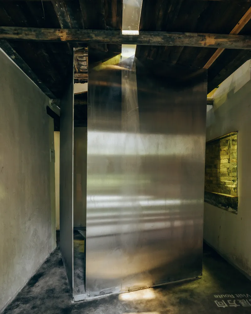 Brass wall panel rising through exposed timber ceiling joists with light from above