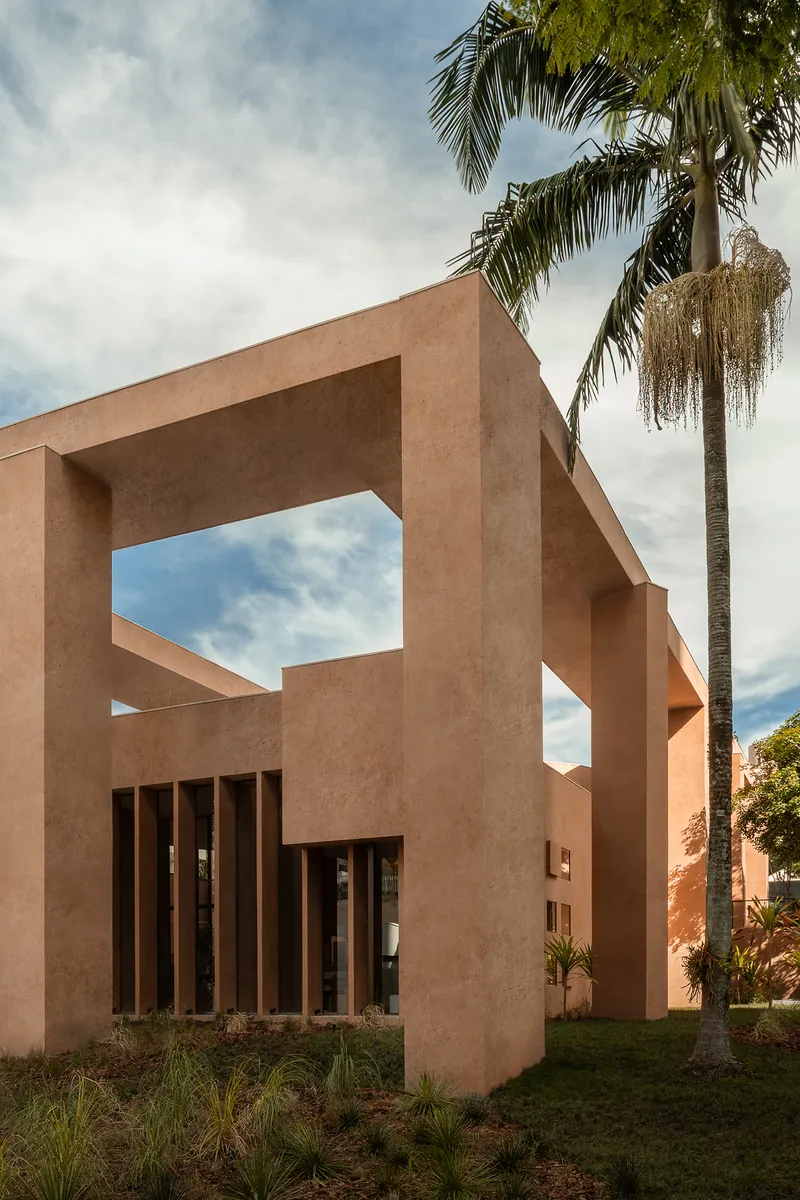 Upward view of terracotta columns supporting angled concrete beams beneath a palm tree