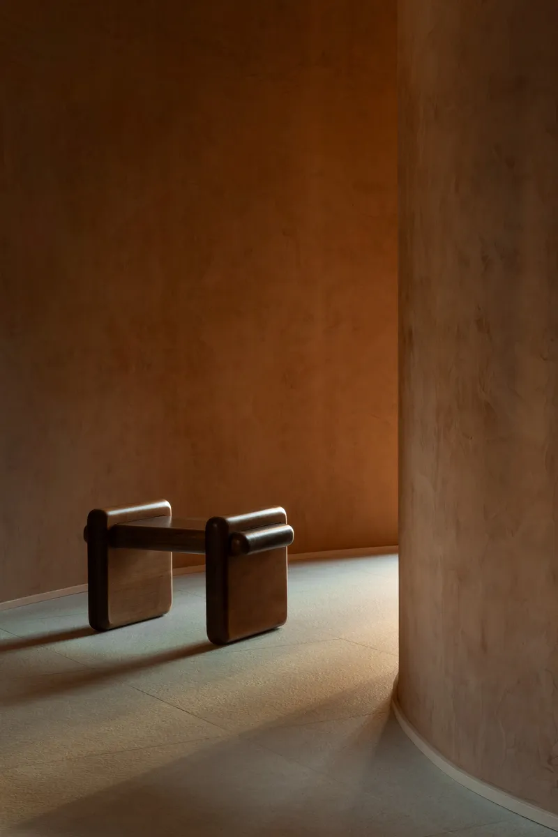 Interior corner with curved terracotta walls and two upholstered stools in warm afternoon light