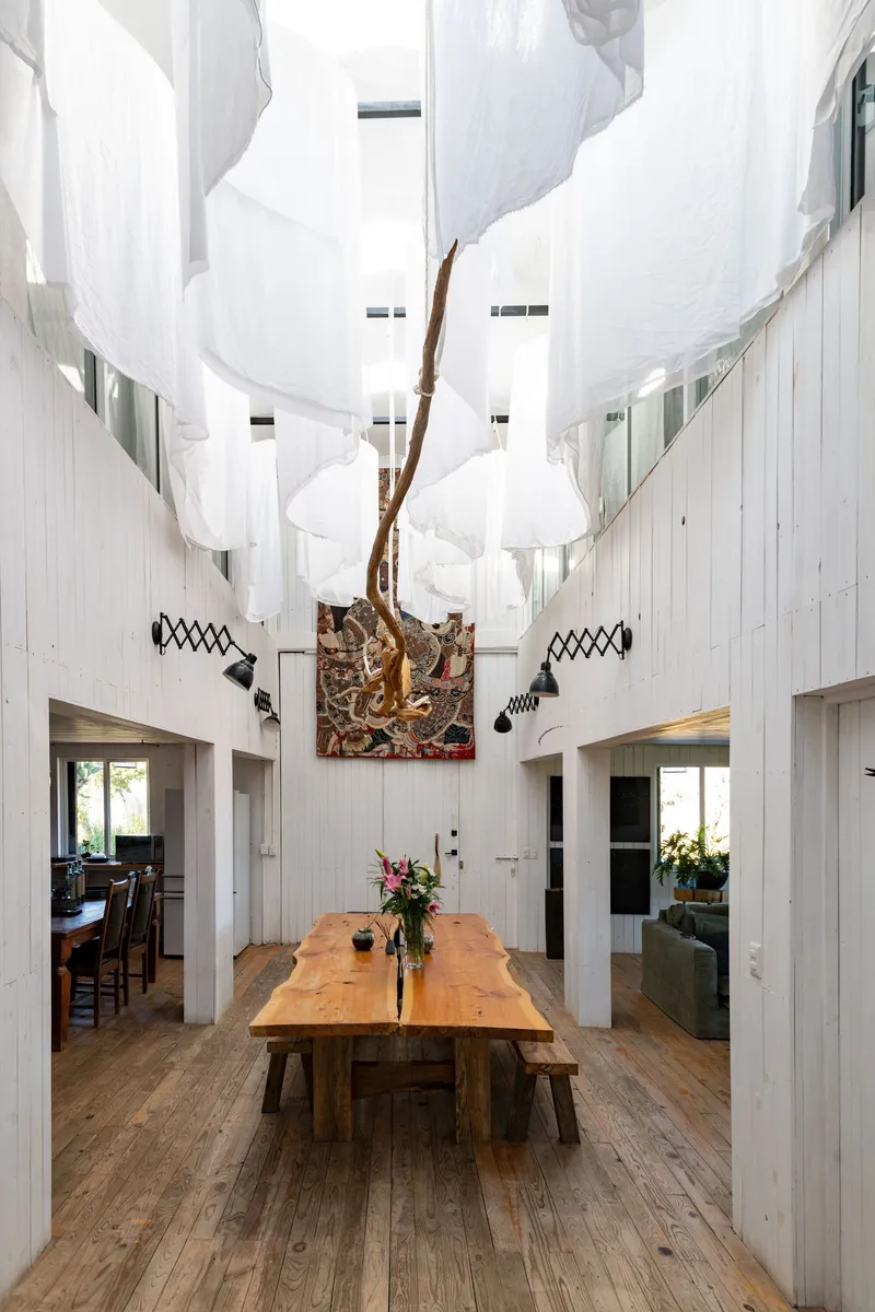 Double-height dining space with whitewashed timber walls, carved tree sculpture and billowing fabric ceiling installation