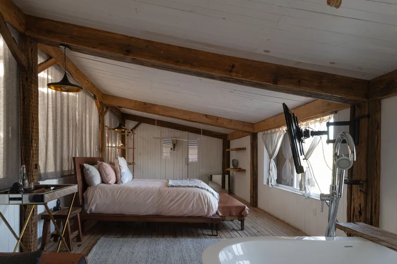 Bedroom interior with exposed timber beams, whitewashed plank ceiling and freestanding bathtub beside the bed
