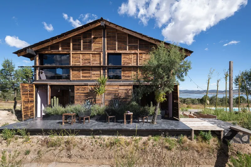 Front elevation showing horizontal wood cladding, operable shutters, and ground-level terrace with potted succulents