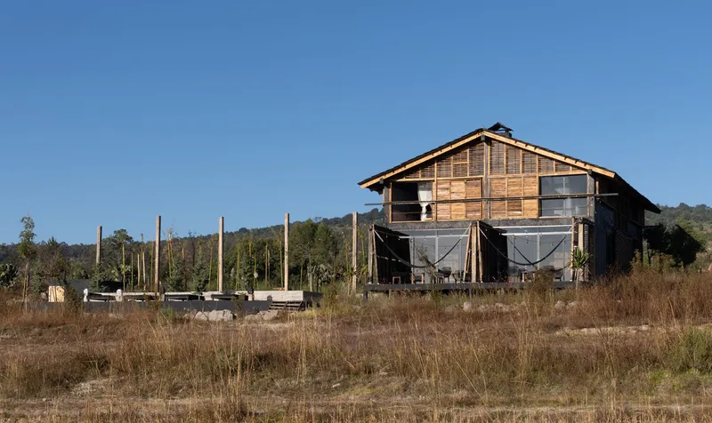 Front elevation showing the gabled timber facade with screened lower porches across a dry grassy field