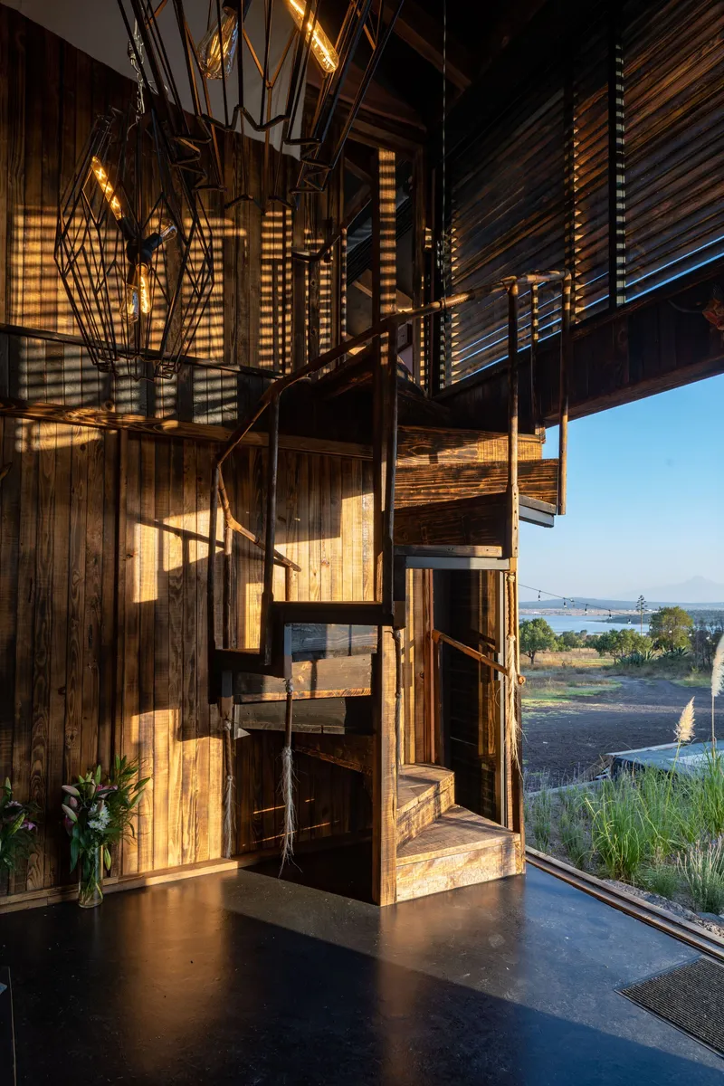 Steel spiral staircase with wire-frame pendant lights casting geometric shadows on timber walls at dusk