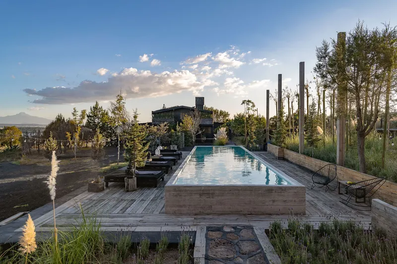 Elevated timber lap pool on deck with planted borders and steel columns at sunset
