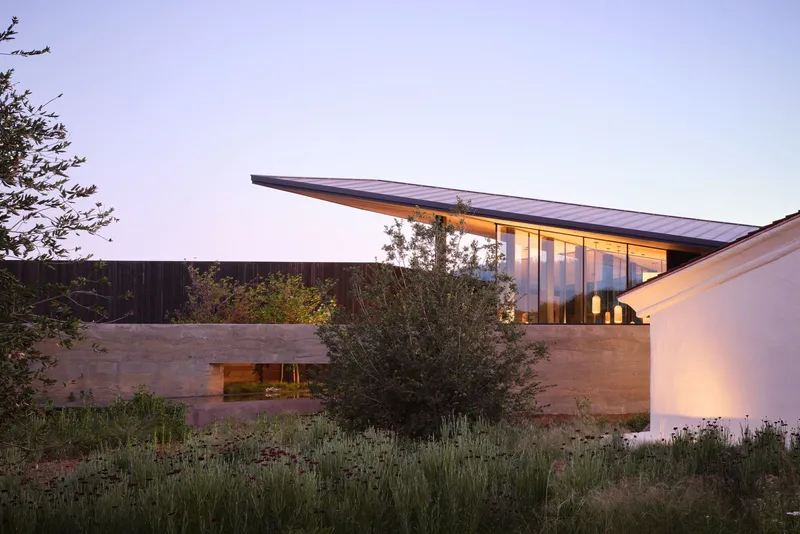 Exterior view of the cantilevered roof and rammed earth walls among drought-tolerant plantings at dusk