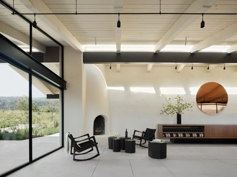 Interior living space with exposed timber ceiling beams, arched fireplace and floor-to-ceiling glazing overlooking the landscape