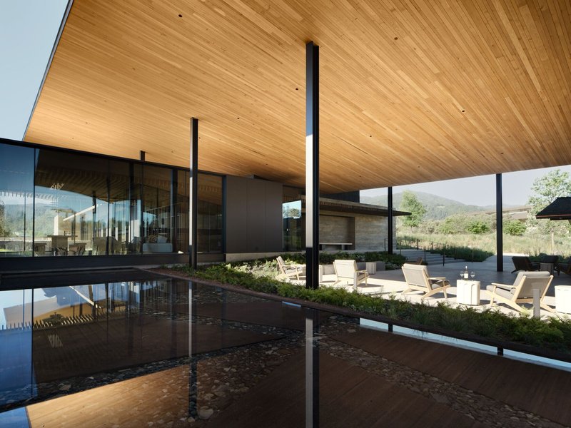 Covered terrace with timber soffit and slender black columns reflected in the pool below