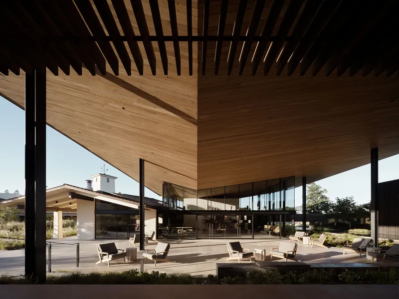 Covered terrace with timber-slatted ceiling and black steel columns framing view of historic chapel beyond