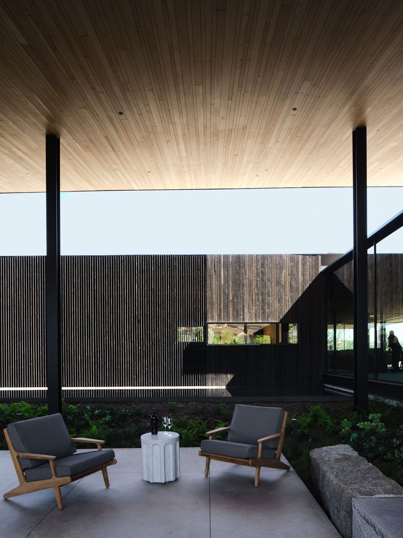 Covered terrace with timber ceiling and black steel columns framing a planted courtyard at dusk