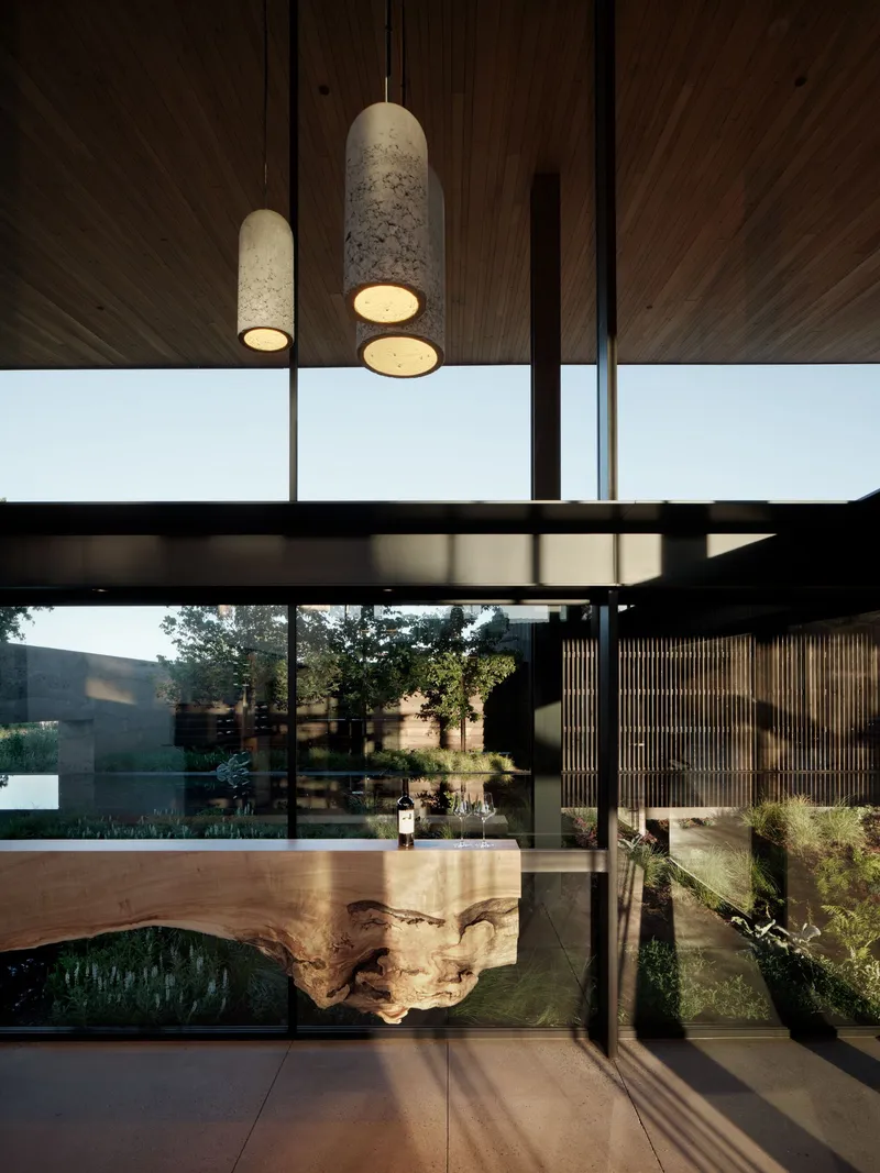 Live-edge wood dining table beneath cylindrical stone pendant fixtures with timber ceiling above