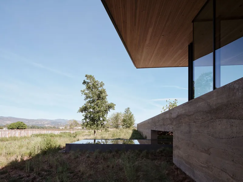 Cantilever timber soffit above board-formed concrete retaining wall overlooking vineyard and distant hills