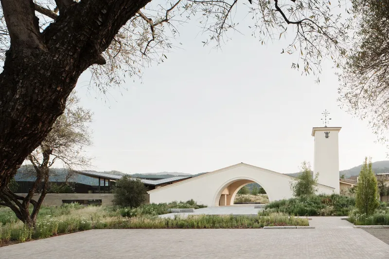 White stucco chapel with bell tower and arched portal seen across native grass plantings
