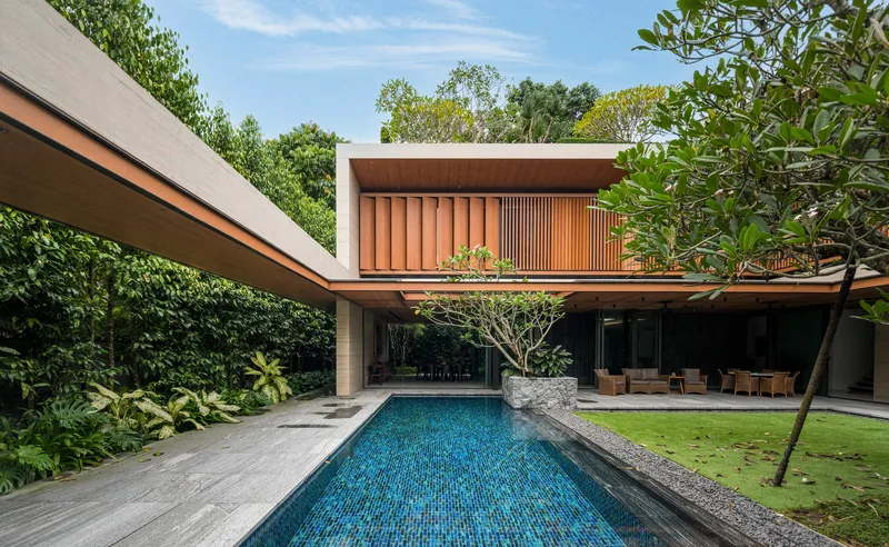 Blue mosaic-tiled pool extending toward timber-clad volumes with glass walls and planted roofs