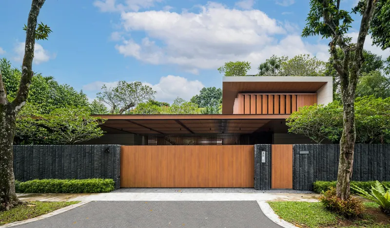Street facade with timber cladding and dark stone boundary wall beneath a partly cloudy sky