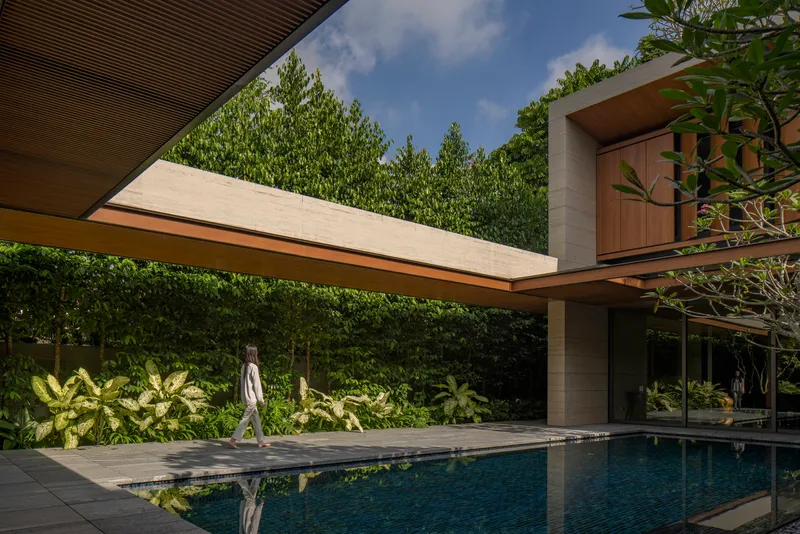Pool terrace with a figure walking past dense plantings beneath cantilevered concrete and timber volumes