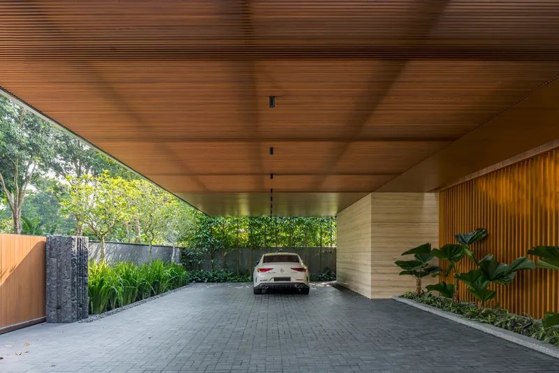 Covered carport with slatted timber ceiling and stone-clad columns framing a vehicle entrance