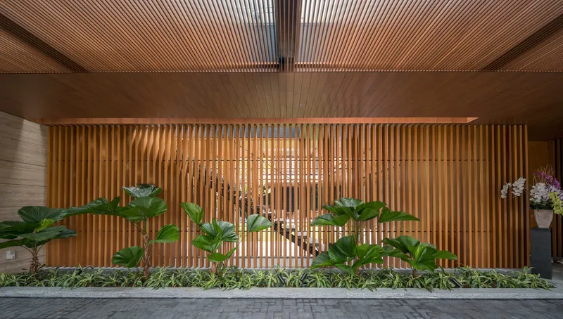 Entry facade with vertical timber screen and planted bed of broad-leafed palms at dusk