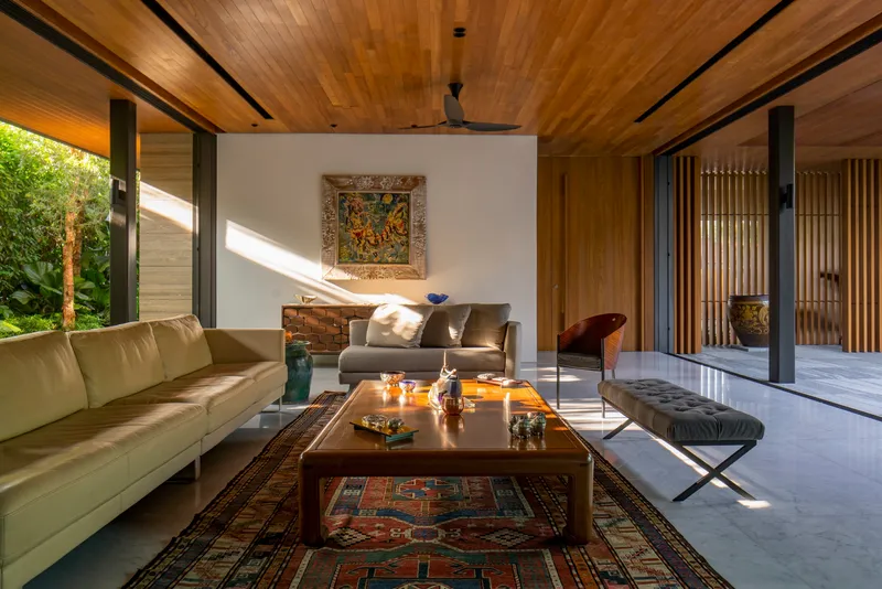 Living room with timber ceiling and full-height glazing opening to a garden courtyard in afternoon light