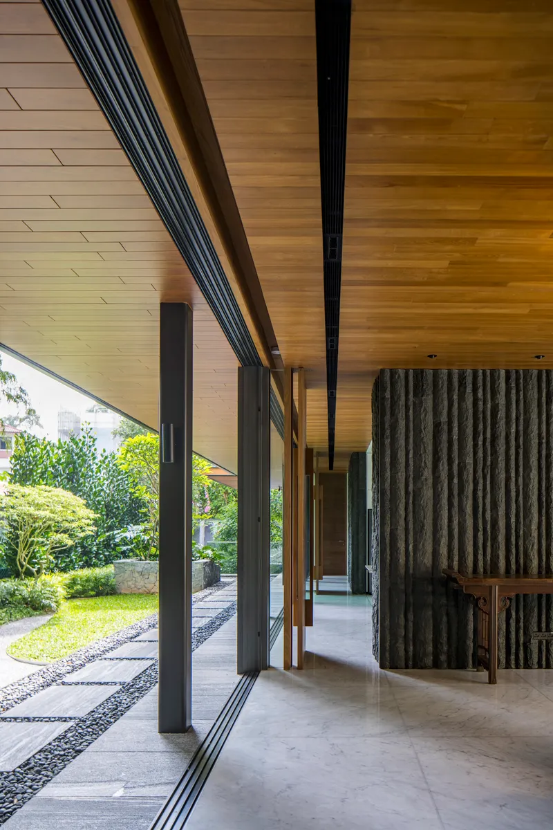 Covered walkway with timber-clad soffit and concrete flooring alongside a gravel garden path