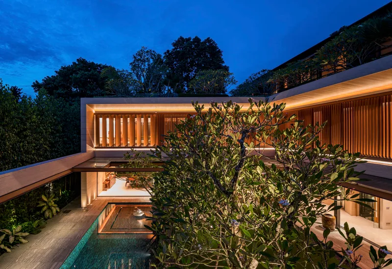 Upper level terrace with vertical timber louvers and rooftop garden visible through frangipani canopy at twilight