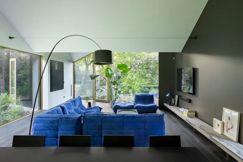 Living room with floor-to-ceiling glazing opening to a garden with trees and filtered daylight