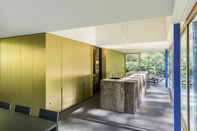 Open kitchen with brass storage wall and stone-clad island beneath a white ceiling plane