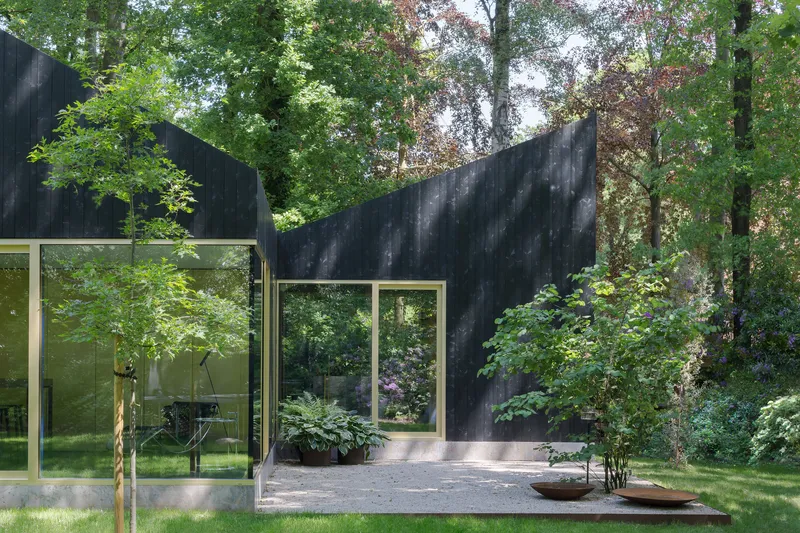 Courtyard entry with charred timber wall, planted beds and tall grasses framing glazed threshold