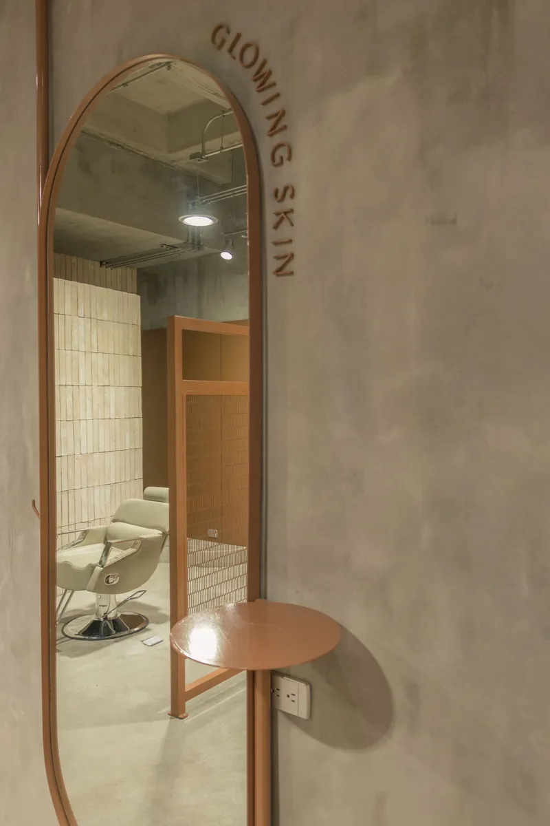 Oval mirror with integrated copper shelf and branded lettering on concrete wall