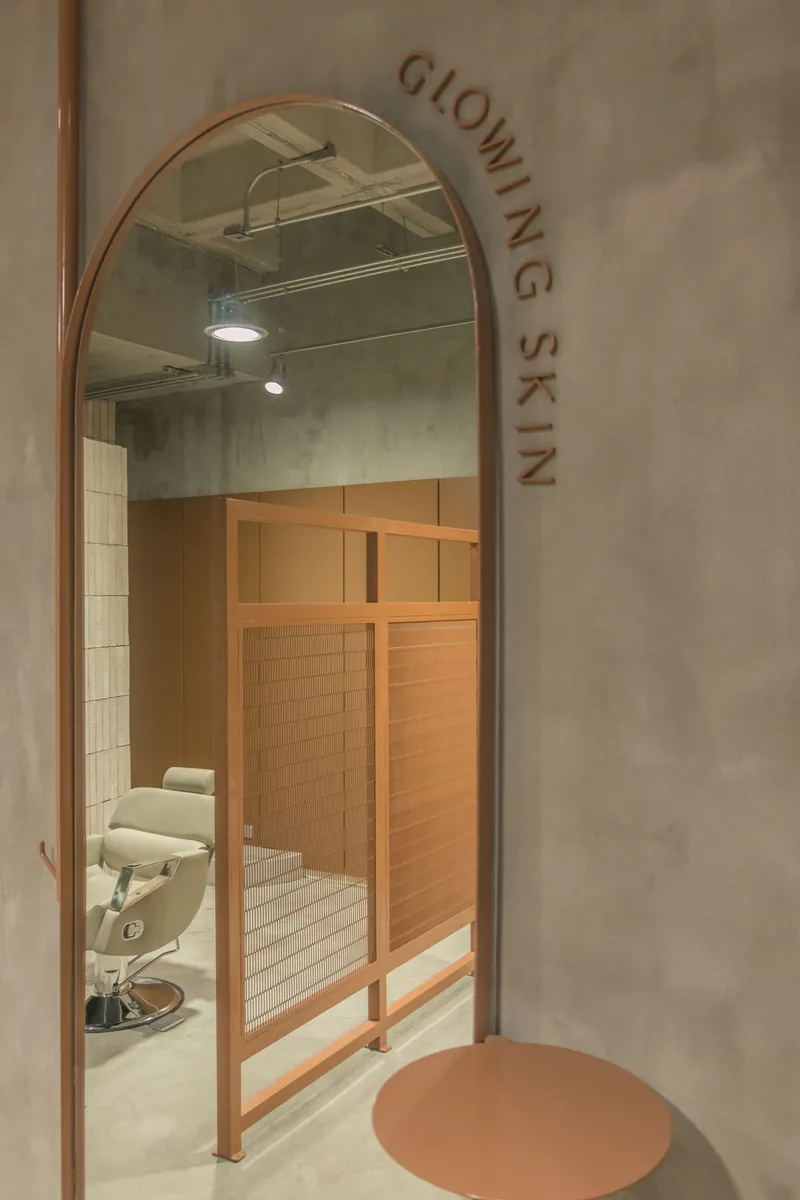 Copper arched mirror reflecting salon station through doorway with lettering on grey plaster wall
