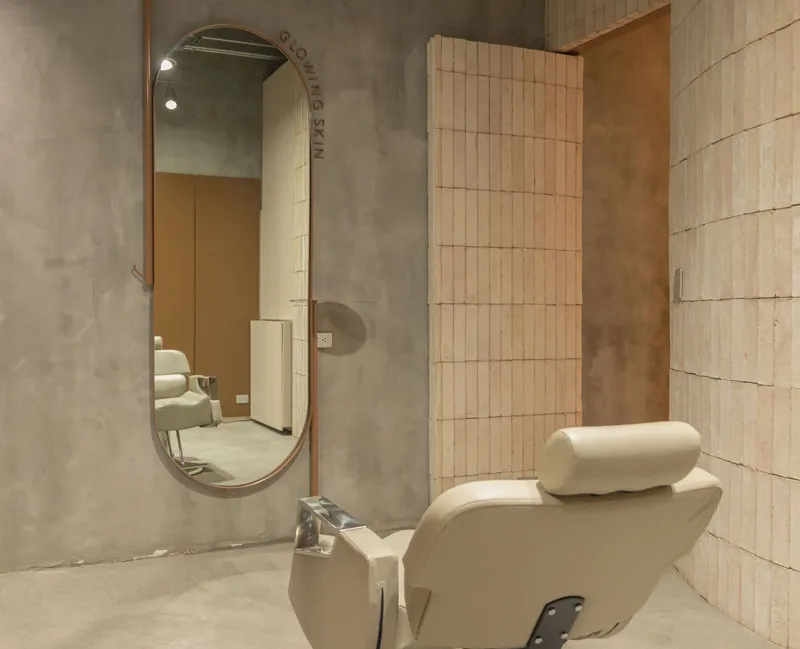 Reclined salon chair with oval mirror and vertical tile wall under exposed ceiling conduits