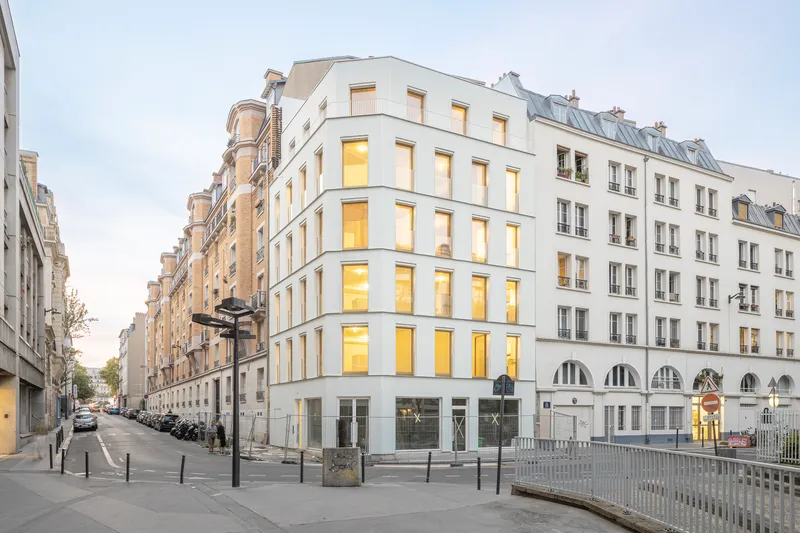 Corner view of the white facade with inset windows and arched ground floor openings at dusk