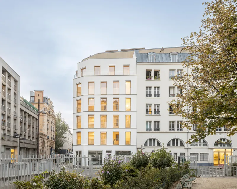 Street facade with vertical window bands and planted courtyard in front under autumn trees
