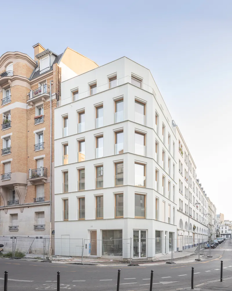 White facade with recessed timber-framed windows wrapping around the street corner at daylight