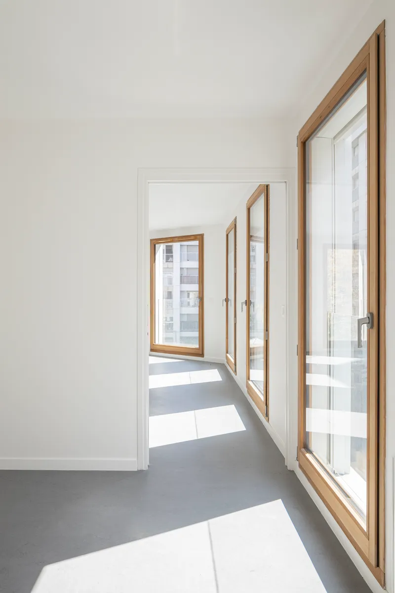 Corridor with timber-framed casement windows creating angled patches of sunlight on the grey floor