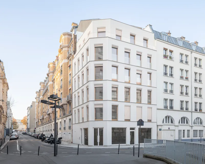 Six-story residential corner building with white rendered facade and arched ground floor openings beside street with parked motorcycles