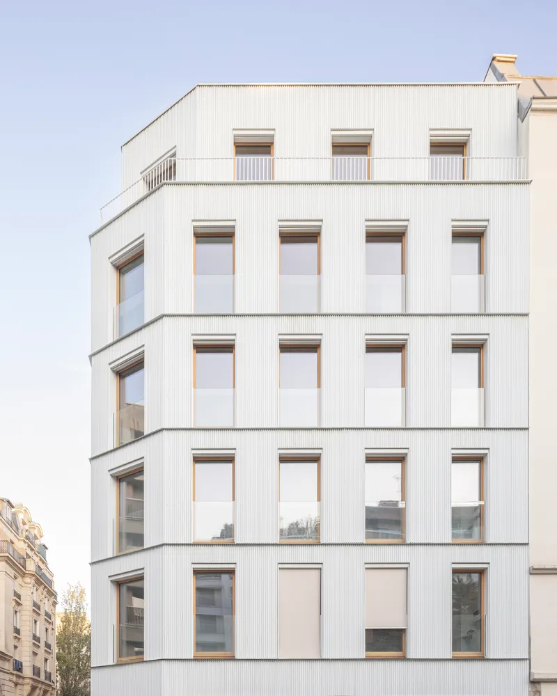 Facade detail showing vertical corrugated cladding panels with timber-framed windows in a regular grid