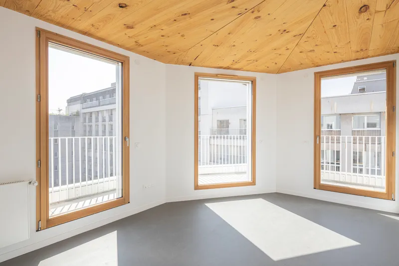 Corner room interior with three timber-framed windows and a plywood plank ceiling in daylight