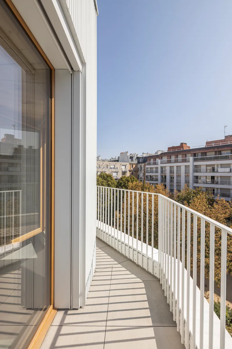 Curved balcony with white vertical metal railings overlooking treetops and neighboring buildings in daylight