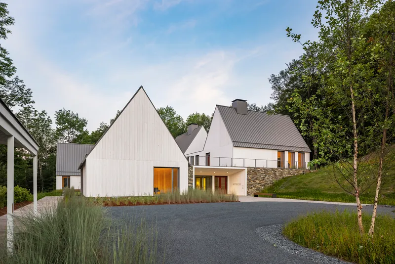 Entry courtyard view of white vertical-board gabled buildings with stone base walls at dusk